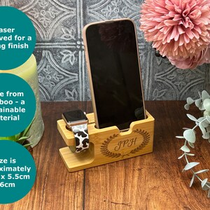 May include: A wooden phone and watch stand with a personalised inscription "IPH" in a laurel wreath design. The stand is made from bamboo and measures approximately 14 cm x 5.5 cm x 6 cm.