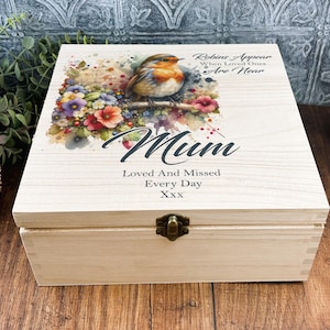 May include: A light-coloured wooden box with a hinged lid. The lid features a watercolour painting of a robin perched on a branch with flowers. Text on the lid reads "Mum, Loved And Missed Every Day". A metal clasp secures the box.