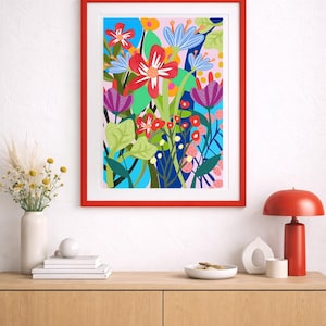 Puede incluir: Una impresión artística floral enmarcada con un diseño vibrante y colorido. La obra presenta una variedad de flores estilizadas en tonos de rojo, azul, morado y verde, sobre un fondo rosa claro y azul. La impresión está encerrada en un marco rojo brillante.