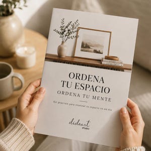 Puede incluir: Una persona sostiene un folleto blanco con el texto "ORDENA TU ESPACIO" y "ORDENA TU MENTE". El folleto presenta un diseño minimalista con una pequeña ilustración de paisaje y un jarrón con vegetación. También se ve la marca "dideart STUDIO".