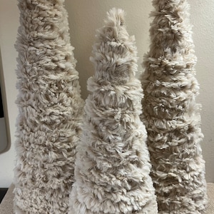 May include: Three fluffy, cone-shaped, white faux fur Christmas trees of varying sizes.