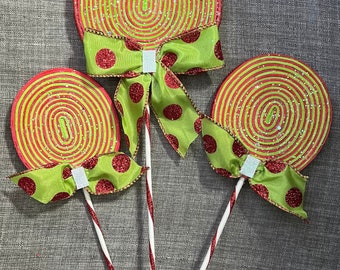 May include: Three red and green lollipop decorations with candy cane sticks and green bows with red polka dots.