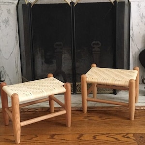 May include: Two wooden stools with woven cane seats. The stools are light brown and have a simple design.
