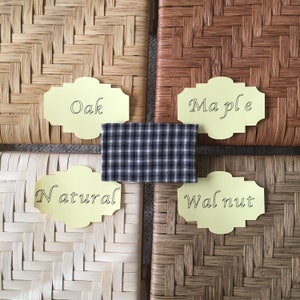 May include: Four woven wood samples labeled with their wood type: Oak, Maple, Natural, and Walnut. The samples are arranged in a square with a black and white checkered fabric in the center.