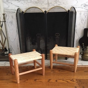 May include: Two small wooden stools with woven cane seats. The stools are in front of a black fireplace screen.
