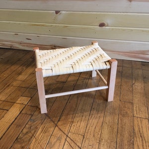 Peut inclure: Un petit tabouret en bois avec un siège en osier. Le tabouret est en bois clair et a un design simple.