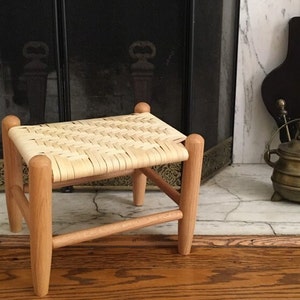 May include: A small wooden stool with a woven seat. The stool is made of light wood and has a simple design.