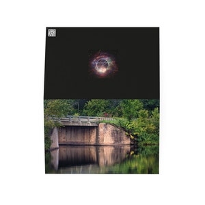 May include: A stone bridge over a calm body of water with lush green trees on either side. The water reflects the trees and the sky, creating a serene scene.