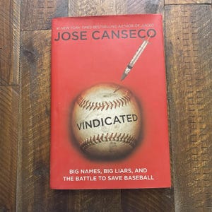 May include: A red book titled Vindicated by Jose Canseco, #1 New York Times bestselling author of Juiced. The cover features a baseball with a syringe pointing toward it and the subtitle Big Names, Big Liars, and the Battle to Save Baseball.