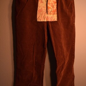 Puede incluir: Un pantalón de pana marrón con un parche de tela floral cosido en la parte delantera.