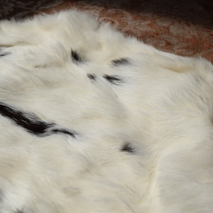 May include: A white cowhide rug with black patches. The rug has a soft, fluffy texture.