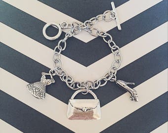 May include: A silver charm bracelet with three charms: a dress, a purse, and a high heel shoe.