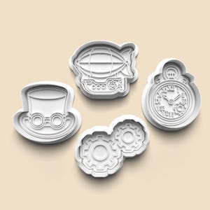 Puede incluir: Cuatro cortadores de galletas de plástico blanco con temática steampunk. Los diseños incluyen un sombrero de copa con gafas, un dirigible, un reloj de bolsillo y dos engranajes entrelazados. Los cortadores están dispuestos sobre una superficie beige claro.