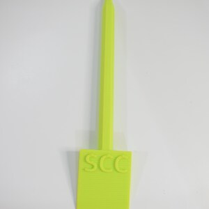May include: A neon green plant tag with the letters "SCC" on the rectangular label. The tag has a long, pointed stem for insertion into the soil. The tag is made of plastic.
