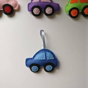 May include: Felt car ornaments in pink, purple, green, and blue. Each car has a ribbon for hanging and features contrasting colors for the wheels and windows. The cars are handmade and suitable for decoration.