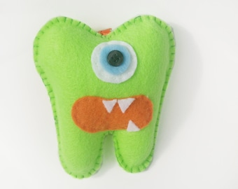 May include: A green felt tooth monster with a single blue eye and an orange mouth with white teeth.