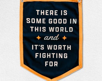 May include: A navy blue banner with the text "THERE IS SOME GOOD IN THIS WORLD and IT'S WORTH FIGHTING FOR" in white. The banner has an orange border and two metal grommets at the top.