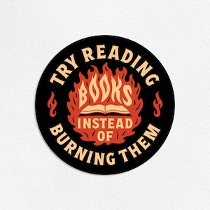 May include: A round black sticker with the text "TRY READING BOOKS INSTEAD OF BURNING THEM" in a cream color. The word "BOOKS" is in the center, inside a flame design. The sticker is a book-themed item.