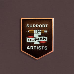 May include: A rectangular badge with a copper-colored border and a dark brown center. The badge features the words "SUPPORT HUMAN ARTISTS" in white, with a stylized pencil and fist graphic. The background is a solid, dark brown.