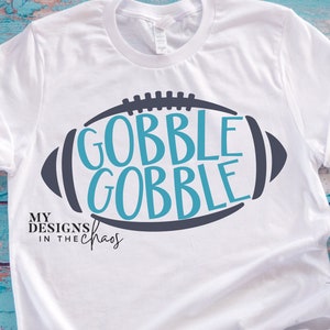 May include: White t-shirt with a blue and gray football design. The football has the words "Gobble Gobble" inside. The text "My Designs in the Chaos" is below the football.