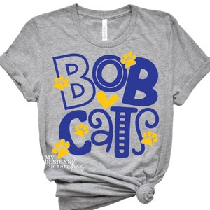 May include: Gray t-shirt with a blue and yellow graphic that says "Bobcats" with paw prints and a heart.