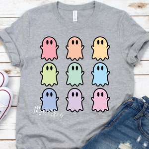 Könnte beinhalten: Ein graues T-Shirt mit einem Design aus neun pastellfarbenen Geistern. Die Geister sind in drei Reihen zu je drei angeordnet. Der Text "My Designs in the Chaos" ist in der linken unteren Ecke des Shirts gedruckt.