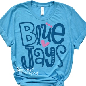 May include: A light blue t-shirt with the text "Blue Jays" in navy blue with a pink heart. The text "My Designs in the Chaos" is in black at the bottom of the shirt.