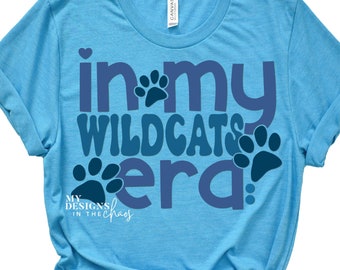 May include: A light blue t-shirt with the text "in my Wildcats era" in navy blue with paw prints. The text "My Designs in the Chaos" is in white at the bottom.