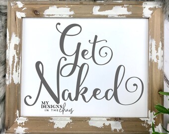 Puede incluir: Un cartel blanco con el texto "Get Naked" en una fuente cursiva gris. El cartel está enmarcado en un marco de madera desgastado con pintura blanca. El texto "My Designs in the Chaos" está en una fuente más pequeña debajo del texto principal.