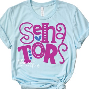 May include: Light blue t-shirt with the text "Senior" in pink with a blue heart and "TORS" in pink with blue polka dots. The text "My Designs in the Chaos" is in black below the main text.