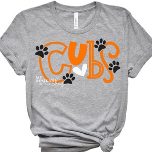 May include: Gray t-shirt with the word "CUBS" in orange with paw prints and a heart. The text "MY DESIGNS IN THE CHAOS" is written below the word "CUBS".