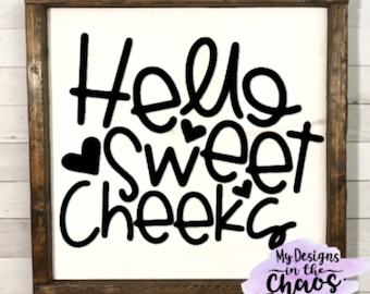 May include: A white wooden sign with black lettering that reads "Hello Sweet Cheeks". The sign is framed in a dark brown wood frame. The text is in a playful, handwritten font. The sign is a great addition to any home decor.
