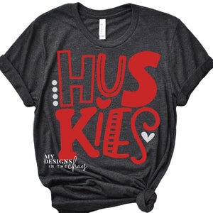 May include: Dark gray t-shirt with the word "Huskies" in red lettering. The word "Huskies" is stylized with a heart and other decorative elements. The text "My Designs in the Chaos" is printed in white at the bottom of the shirt.