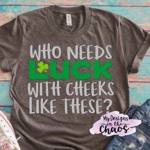 May include: A gray t-shirt with the text "Who needs luck with cheeks like these?" in white and green. The text "luck" has a green shamrock in the "L". The text "My Designs in the Chaos" is in pink and white.