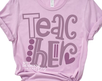 Pode incluir: Uma camiseta lavanda com o texto "Teacher" em fonte roxa. O texto é estilizado com um coração e pontos. O texto "My Designs in the Chaos" está em uma fonte menor na parte inferior da camiseta.