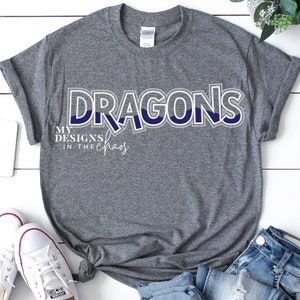 May include: Grey t-shirt with the text "DRAGONS" in a blue and white graphic design. The text "MY DESIGNS IN THE CHAOS" is written in a smaller font below the word "DRAGONS".