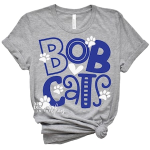 May include: Gray t-shirt with a blue and white design that says "Bobcats" with paw prints.