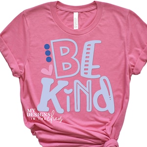 May include: Pink t-shirt with the words "Be Kind" in light blue with a pink heart and blue dots. The text "My Designs in the Chaos" is in black at the bottom of the shirt.