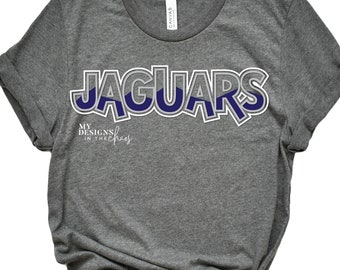 Puede incluir: Camiseta gris con un gráfico azul y blanco que dice "JAGUARS" con el texto "MY DESIGNS IN THE CHAOS" debajo.