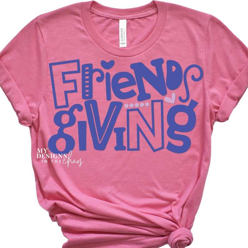 May include: Pink t-shirt with the text "Friendsgiving" in blue lettering. The text is in a playful, stylized font. The shirt is made of a soft, comfortable material.