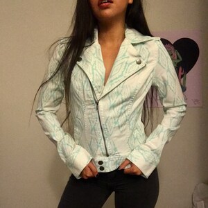 May include: A white denim jacket with a light blue geometric pattern. The jacket has a zipper closure and a collar.