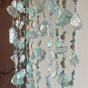 May include: A decorative hanging mobile with clear and seafoam green glass pieces, wire-wrapped and strung with beads. The beads are in various colours and shapes. The mobile is designed for decorative purposes.