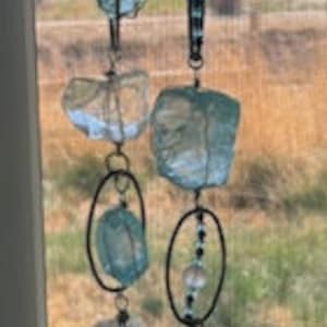 以下が含まれることがあります： 窓から吊るされた青と透明なガラスのクリスタルサンキャッチャーが2つ。それぞれのサンキャッチャーは、ビーズが付いた銀色のチェーンと、上部に銀色のフックが付いています。