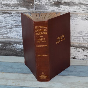 May include: A brown leather-bound book titled "Electrical Engineers' Handbook" by Pender Del Mar, third edition. The book is part of the Wiley Handbook Series and focuses on electric power.