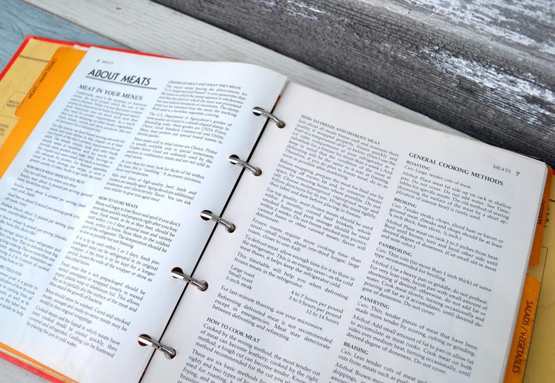 May include: An open cookbook with a yellow tab labelled "Salads/Vegetables" and a white tab labelled "Meats". The page is open to a section titled "General Cooking Methods" with instructions for roasting, browning, pan-broiling, pan-frying, and braising meat.