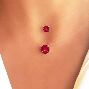 Könnte beinhalten: Eine zarte Halskette mit zwei roten Kristallsteinen, die an einer durchsichtigen Schnur hängen. Die Halskette wird von einer Person mit einem weißen Hemd getragen.