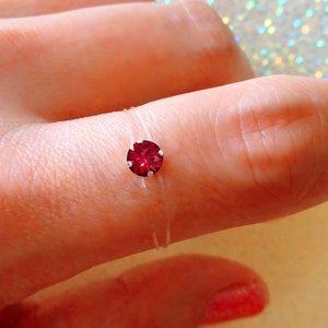 Peut inclure: Une bague en caoutchouc transparente avec un seul strass rouge. La bague est portée sur un doigt.