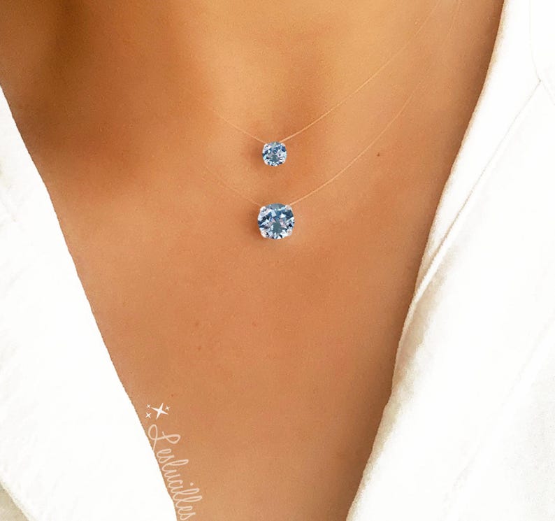 Pode incluir: Um colar delicado de duas camadas com duas correntes finas transparentes e dois pingentes de cristal azul claro. O pingente maior est&aacute; na parte inferior do colar e o pingente menor est&aacute; acima.