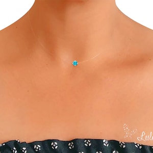 Puede incluir: Un delicado collar transparente con un pequeño colgante de piedra turquesa azul.