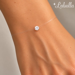 May include: A clear nylon thread necklace featuring a single round brilliant-cut white gemstone centred on the cord. The piece is delicate and minimalist in its construction, showcasing a solitary sparkling stone held by a transparent filament.